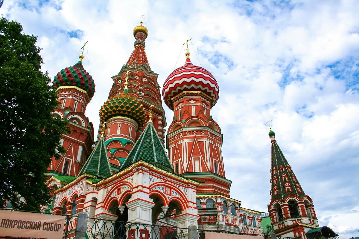 Russian Orthodox church with golden and colorful onion domes against cloudy sky, red brick architecture with ornate details