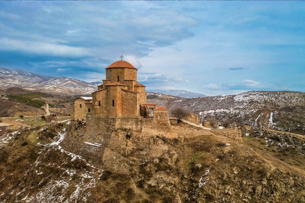 Ancient stone church with golden dome perched on rocky hilltop in snow-covered Caucasus Mountains landscape