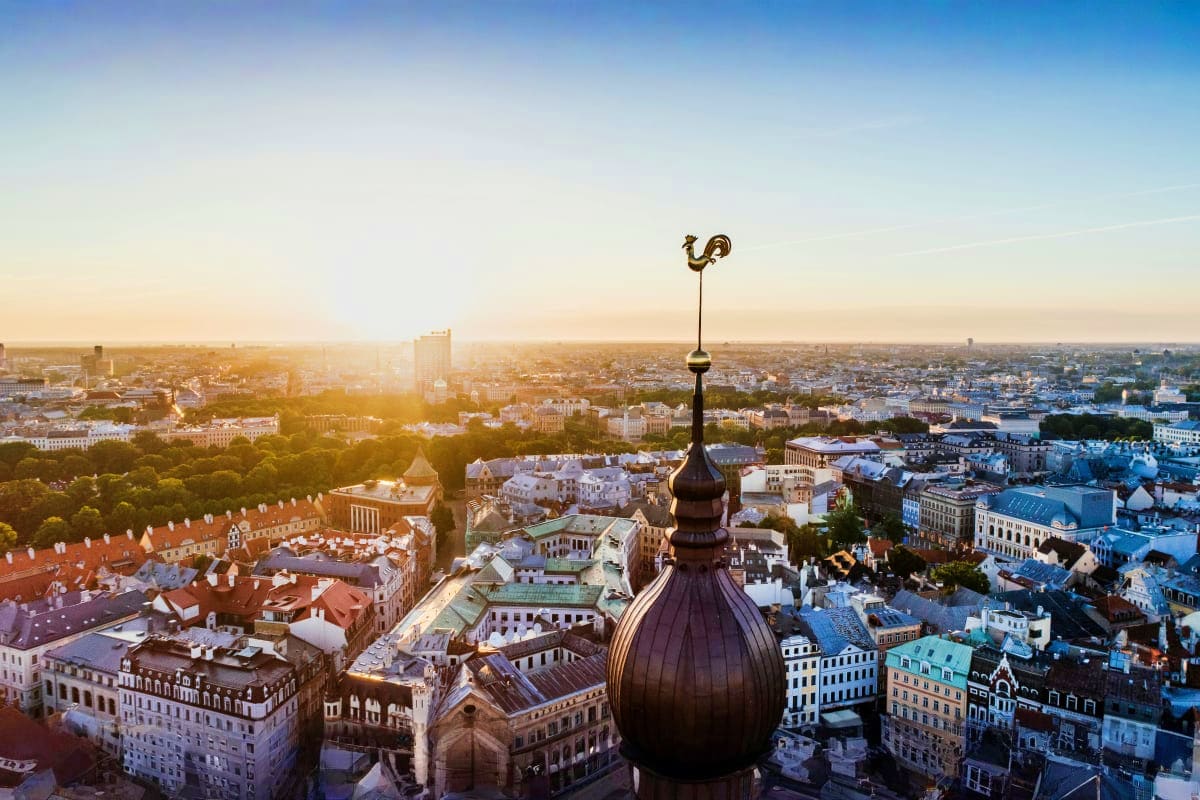 Aerial view of Riga old town at sunset with cathedral dome and cross in foreground, showing historic architecture and citysca