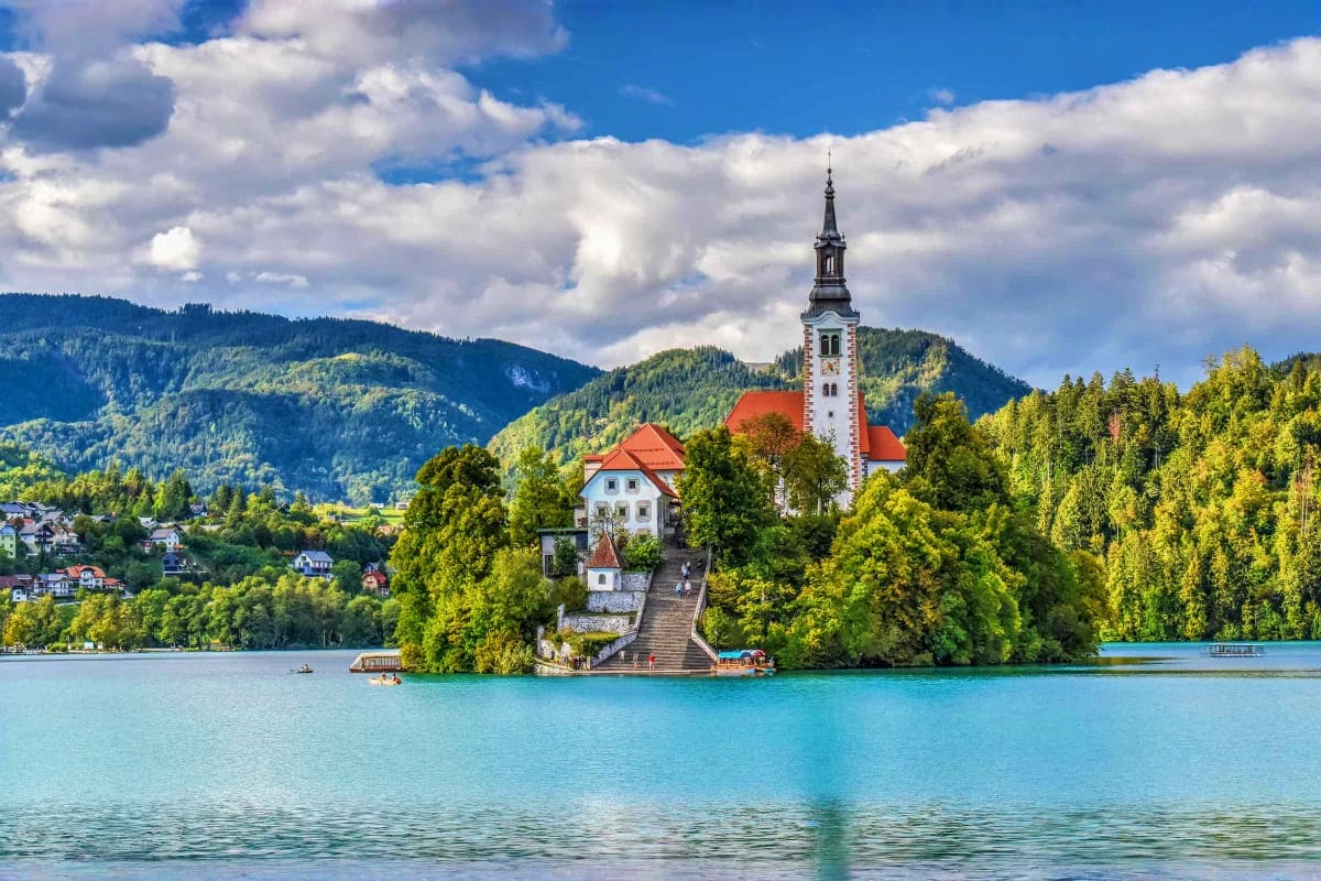 Church with red roof on island in turquoise lake surrounded by forested mountains in Slovenia