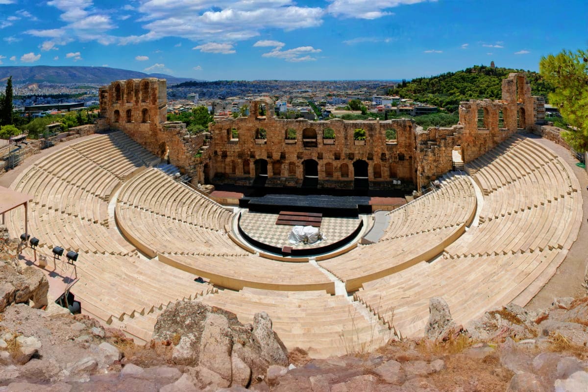 Odeon of Herodes Atticus ancient amphitheater with stone seating and ruins overlooking Athens cityscape on sunny day