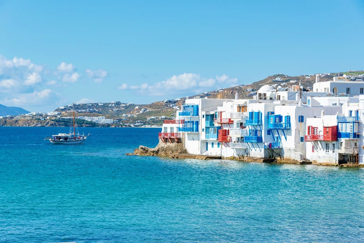 White and blue waterfront buildings in Mykonos, Greece with turquoise sea and traditional wooden boat