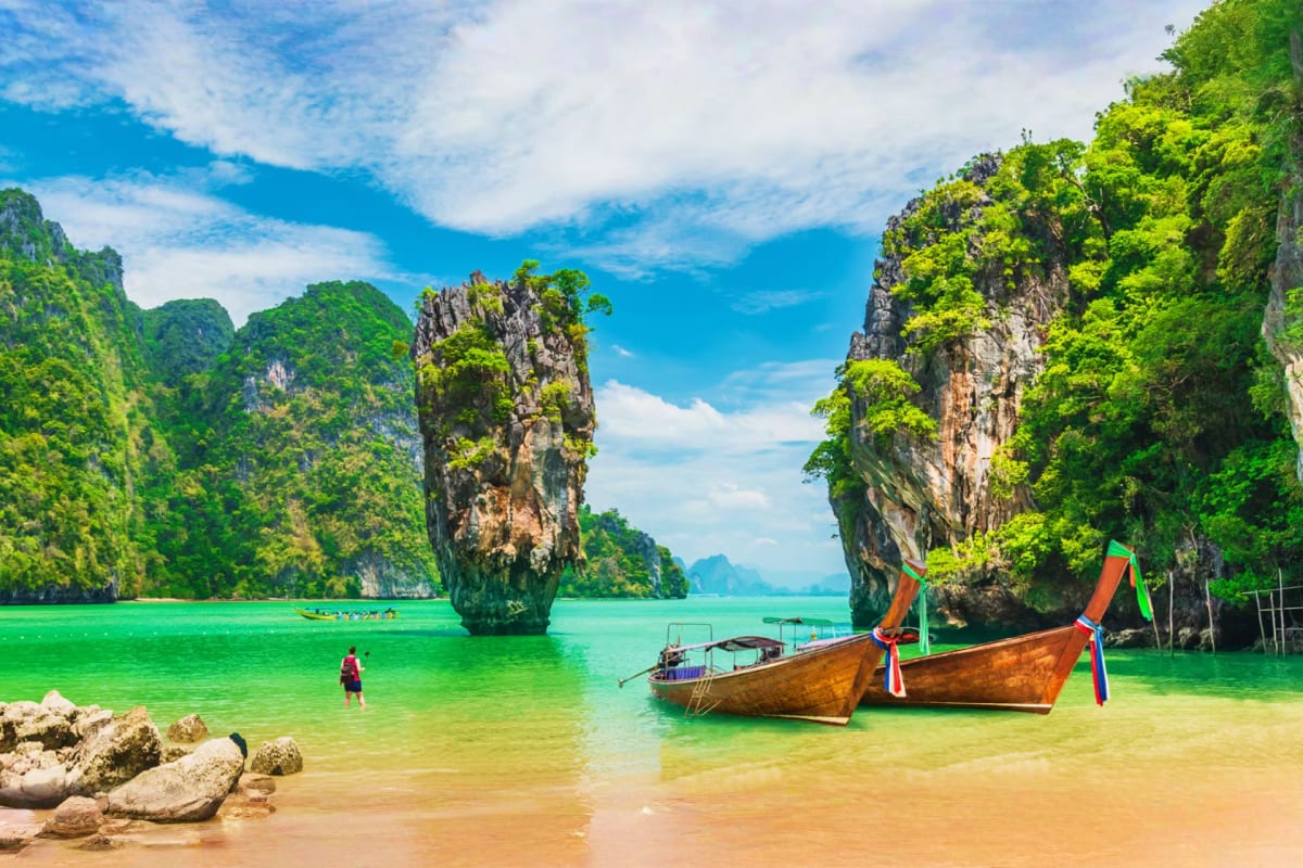 Traditional wooden long-tail boat in turquoise water with limestone cliffs and lush vegetation at James Bond Island, Phang Ng