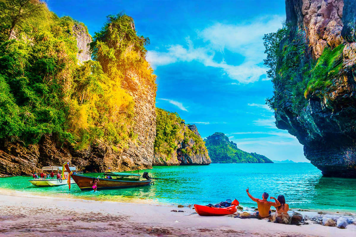 Tropical beach cove in Phuket and Krabi with turquoise water, limestone cliffs, colorful boats, and tourists swimming and rel