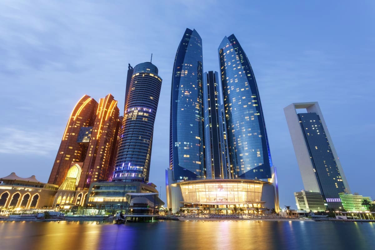 Modern illuminated skyscrapers reflecting in calm waterfront at dusk in Abu Dhabi's downtown skyline