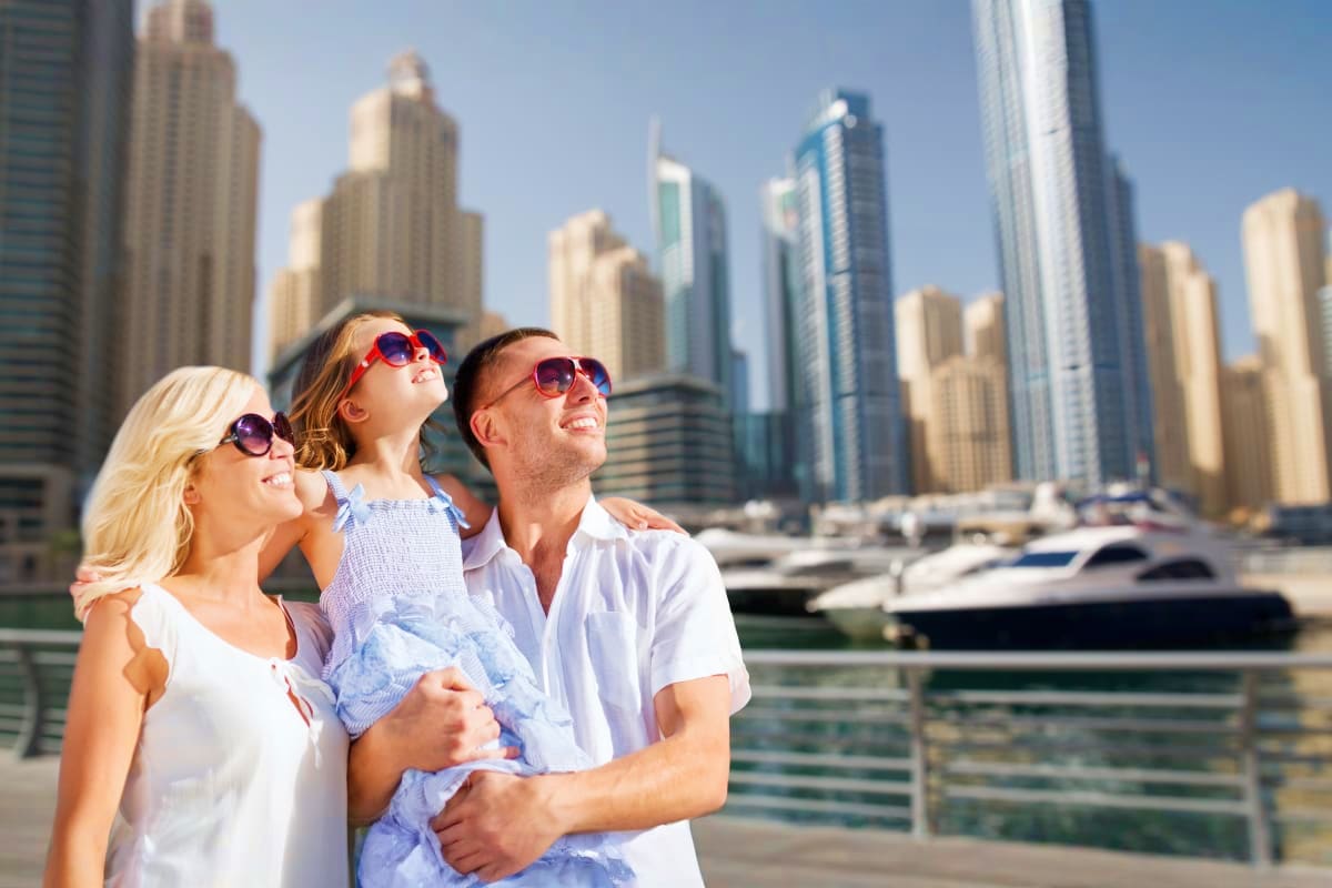 Family wearing sunglasses looking up at Dubai Marina skyscrapers and waterfront with boats