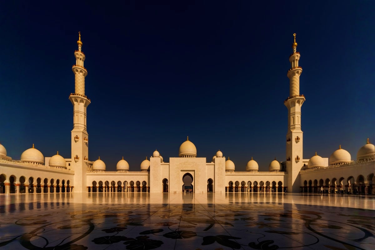 Sheikh Zayed Grand Mosque in Abu Dhabi at dusk with illuminated minarets and courtyard at twilight