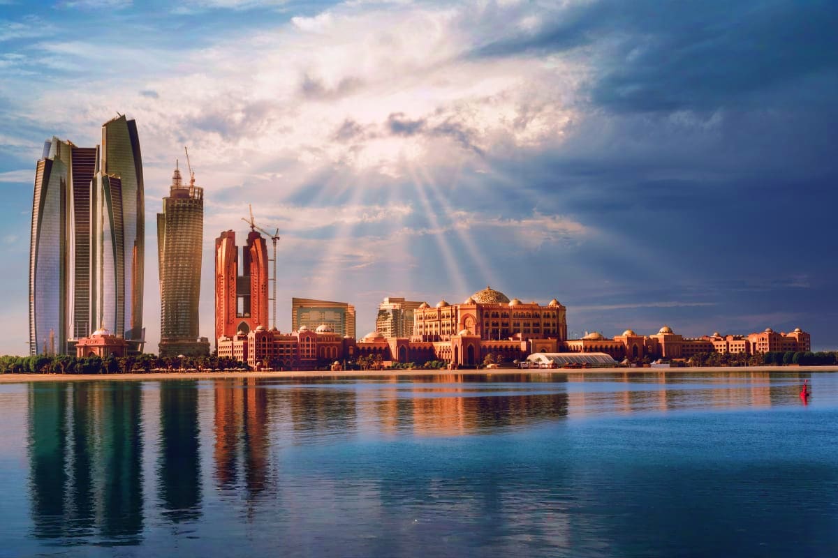 Abu Dhabi skyline with modern skyscrapers and traditional architecture reflected in calm waterfront at sunset with dramatic c