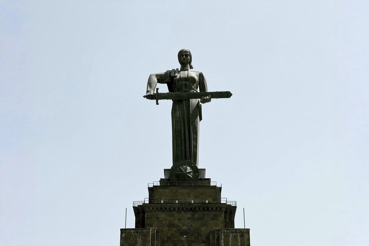 Soviet-era monument featuring a female figure holding a rifle standing atop a stone pedestal against a clear sky