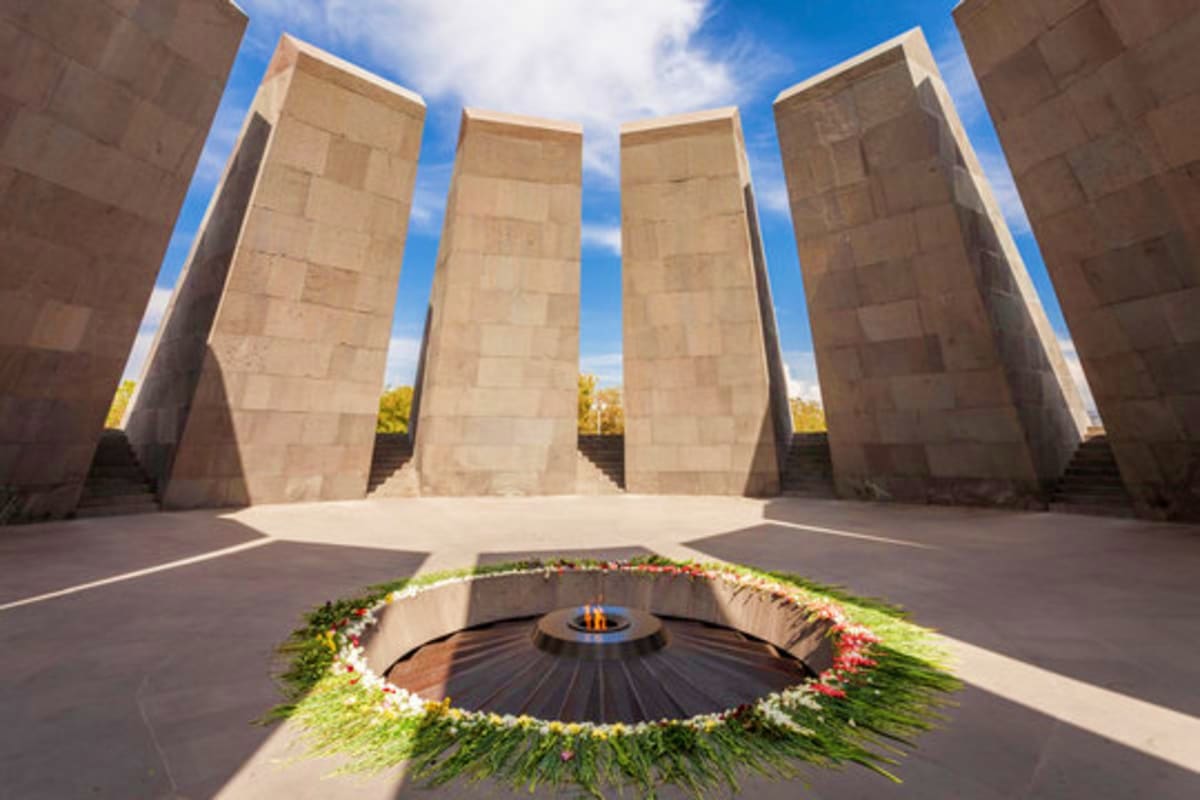 Armenian Genocide Memorial with eternal flame surrounded by flowers and four tall stone slabs against blue sky