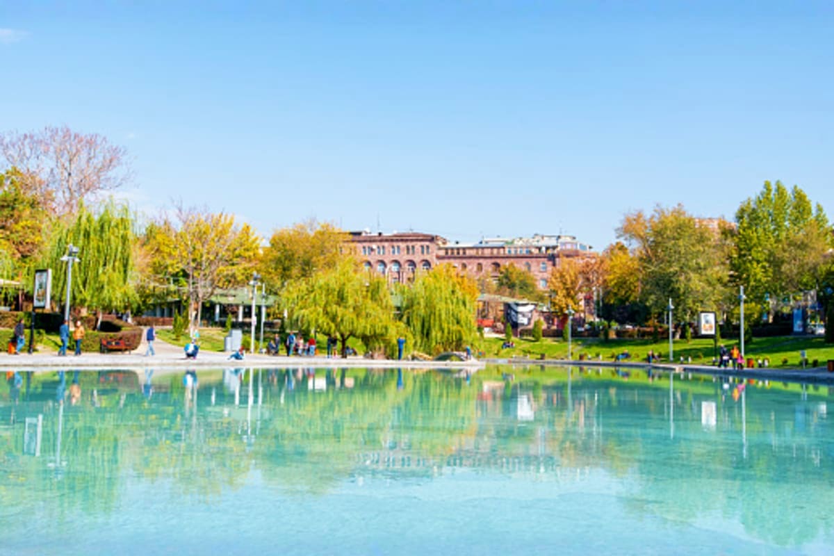 Yerevan waterfront park with turquoise pond, autumn foliage, historic buildings, and visitors enjoying the scenic riverside l