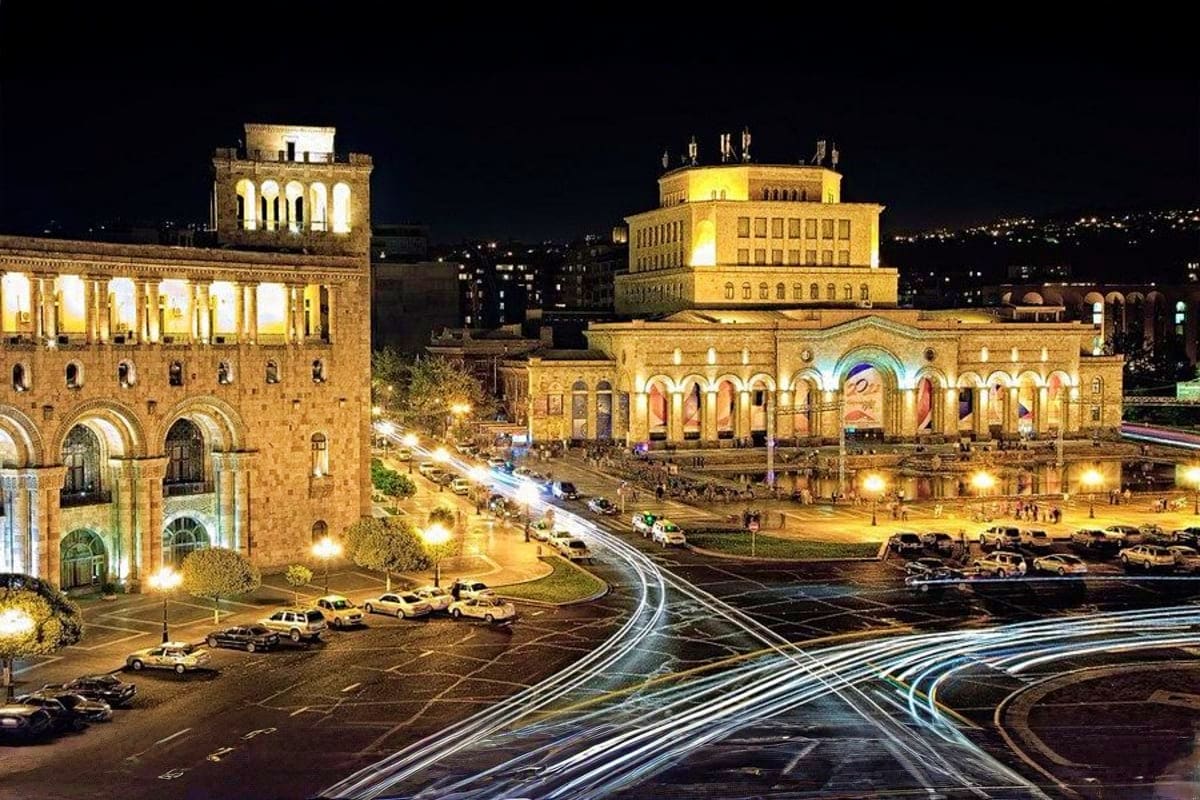 Night view of illuminated Armenian buildings with classical architecture, tram tracks, and parked cars in Republic Square, Ye