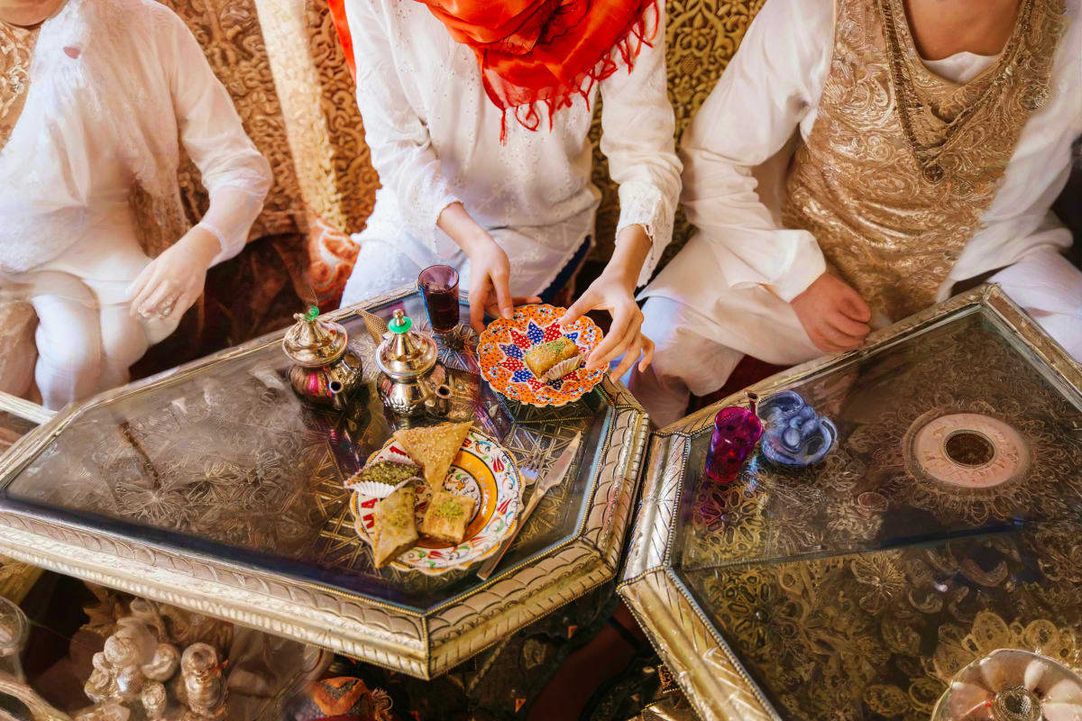 Family in traditional Azerbaijani clothing sharing tea and pastries on ornate table during cultural celebration