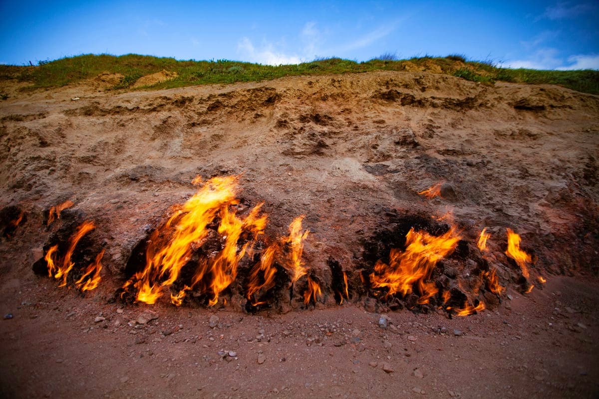 Natural gas flames burning on hillside in Azerbaijan, showing the famous Fire Mountain geological phenomenon with grass-cover