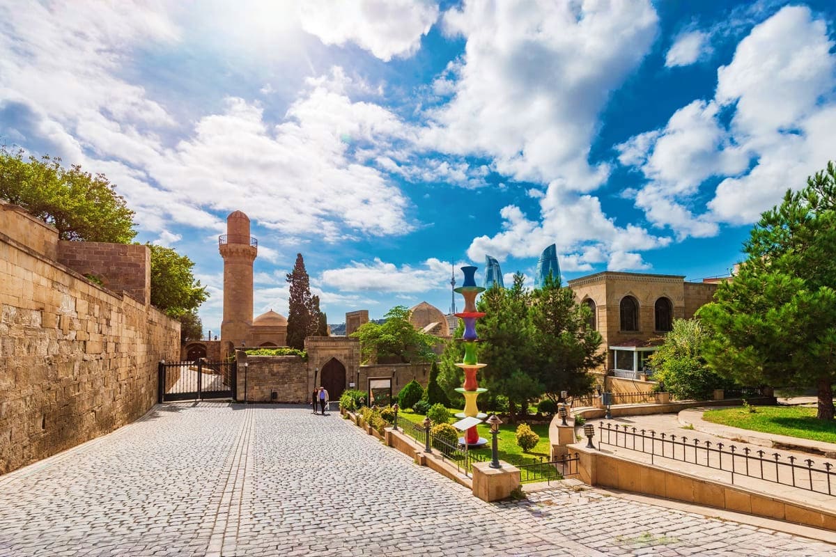 Historic courtyard in Baku with stone walls, minaret, traditional architecture, and colorful modern sculpture under blue sky