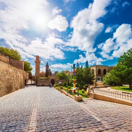 Stone-paved courtyard with historic Islamic architecture, minarets, and blue sky with white clouds in Baku, Azerbaijan