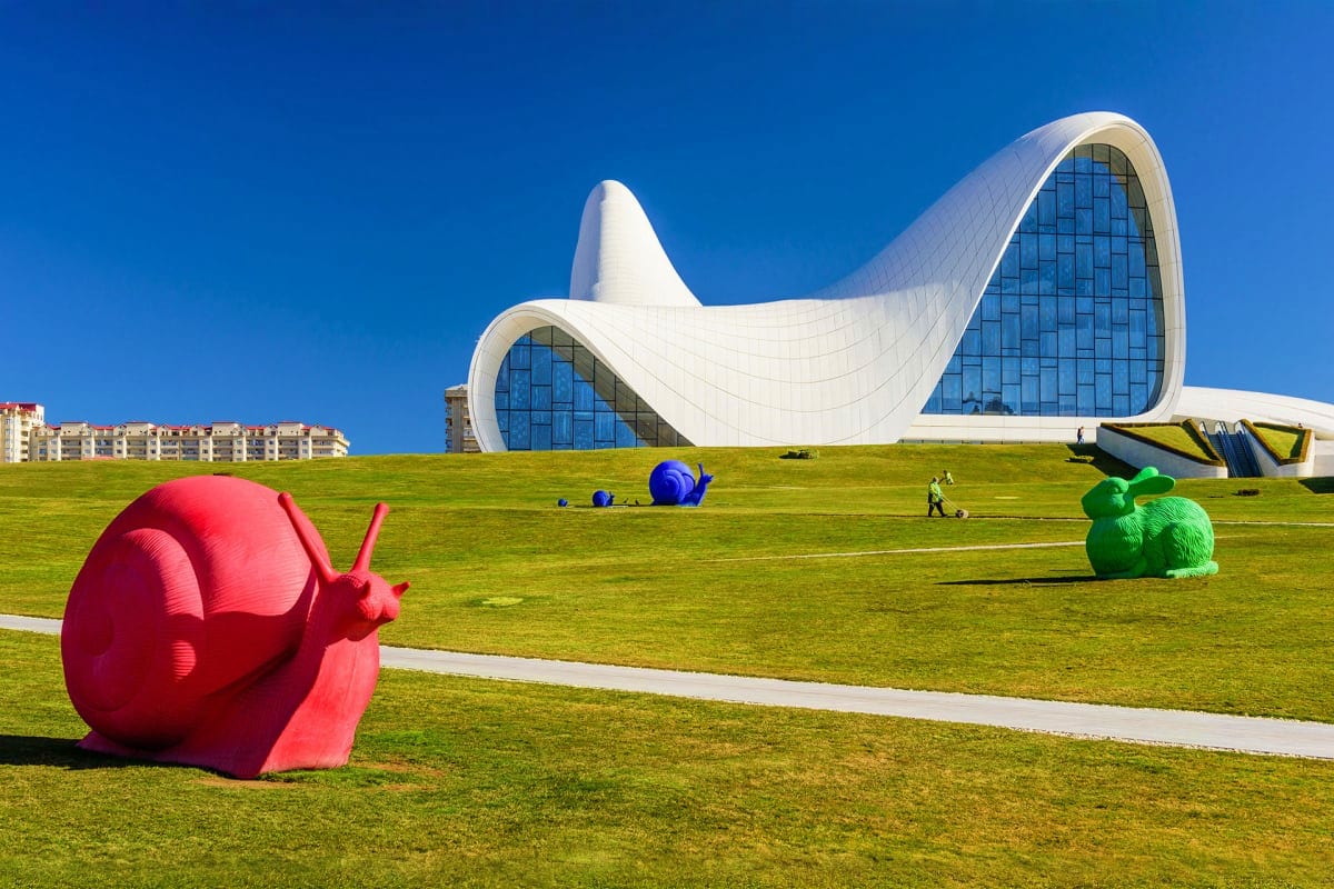 Modern white curved architecture building with colorful snail and animal sculptures on green lawn under blue sky in Baku, Aze