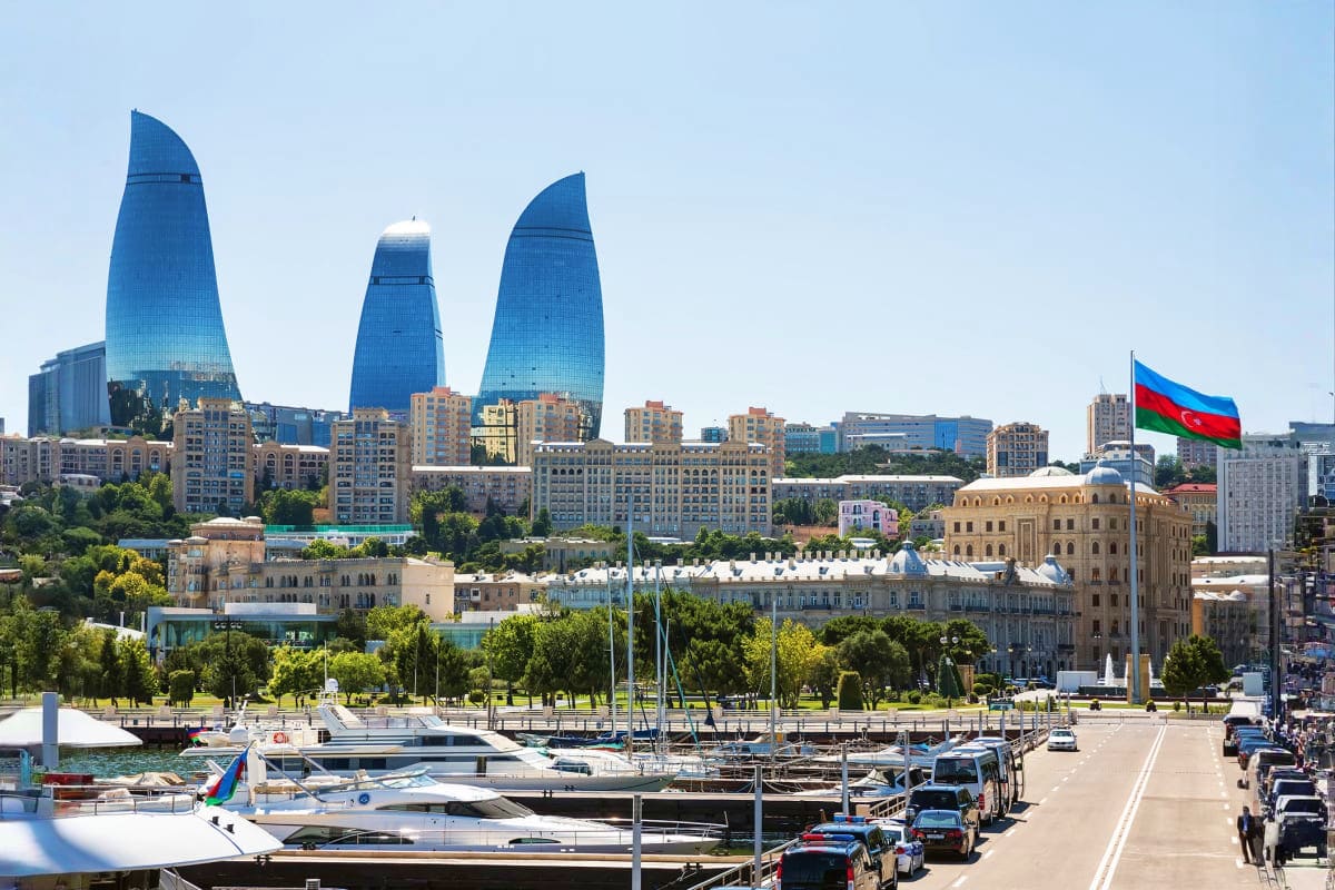 Baku skyline featuring Flame Towers, marina with boats, historic buildings, and Azerbaijan flag overlooking the Caspian Sea w