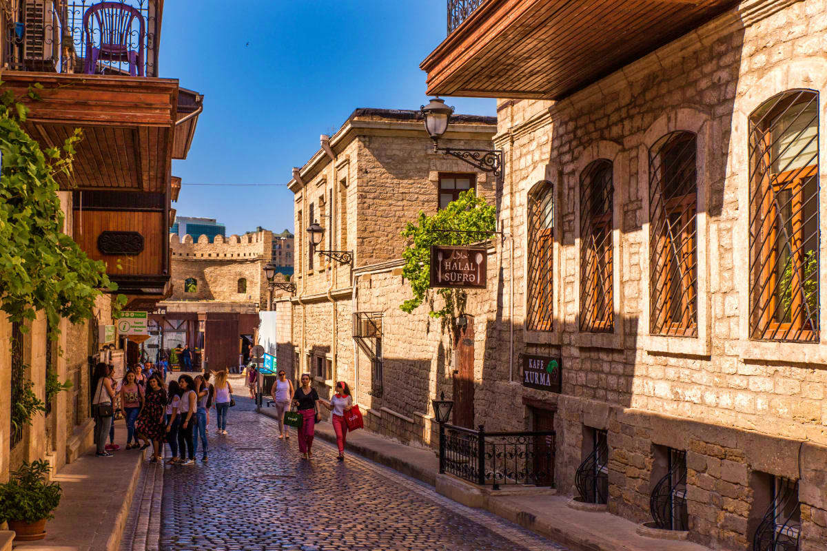 Historic cobblestone street in Baku's old city with stone buildings, wooden shutters, and medieval fortress walls in backgrou