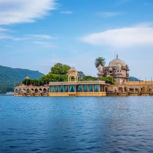 Jag Mandir palace reflected in Lake Pichola waters with green hills and blue sky in Udaipur, Rajasthan