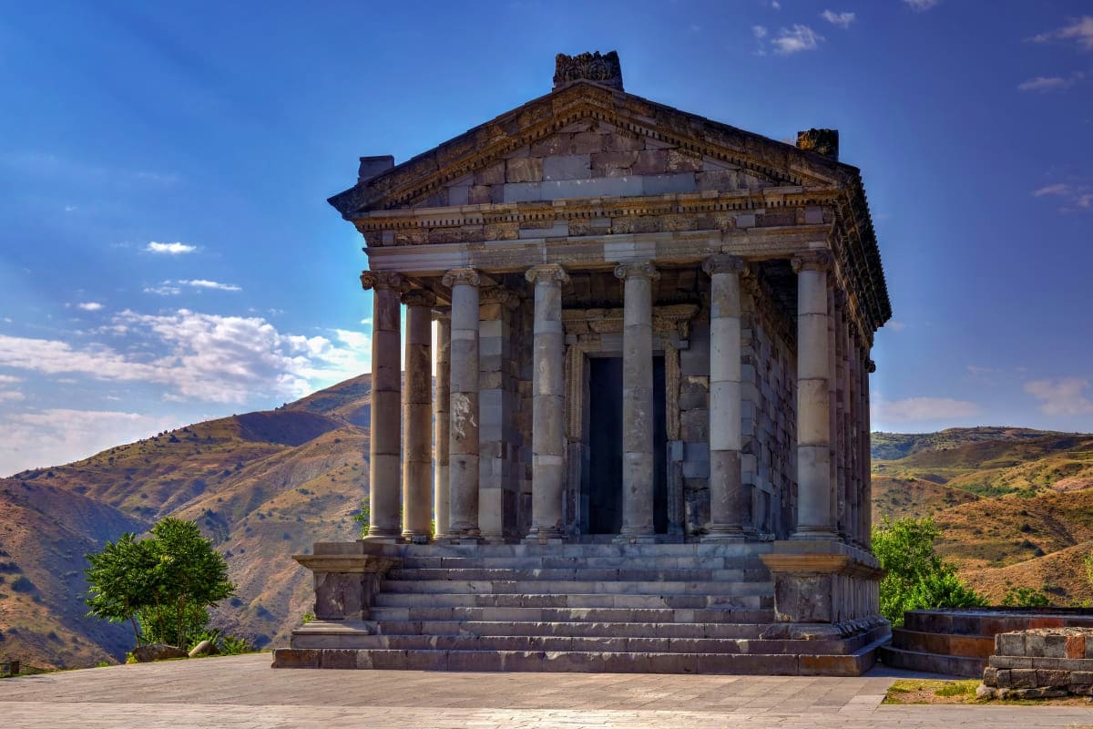 Ancient Greek temple with Corinthian columns overlooking mountainous Armenian landscape under blue sky
