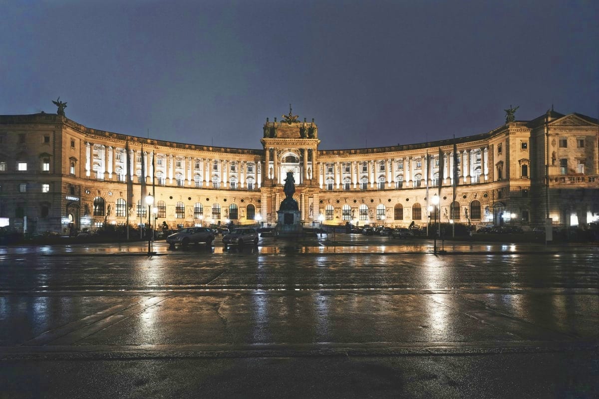 Illuminated Hofburg Palace in Vienna at night with wet plaza and statue, architectural landmark in Austria