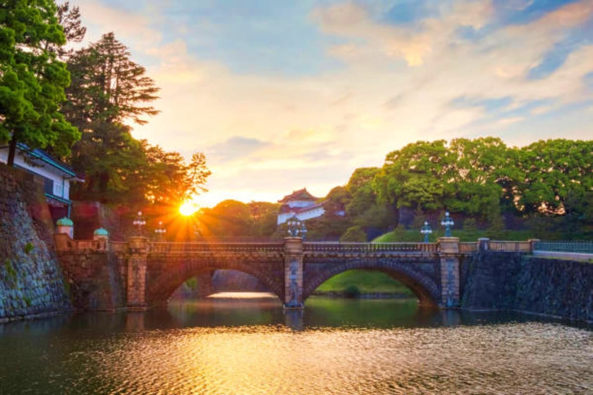 Central Japan Historic stone bridge crossing moat at sunset with traditional Japanese palace and lush green trees in background