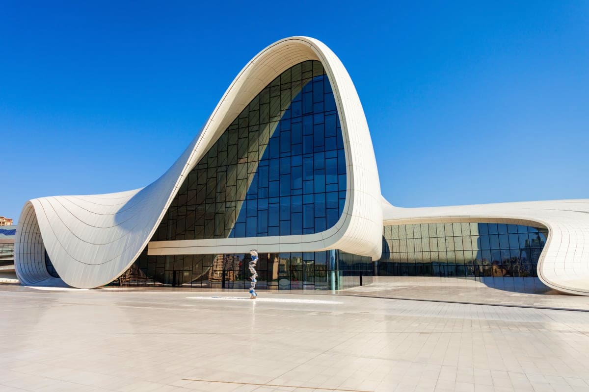 Modern white curved building with wave-shaped architecture and large blue-tinted windows against clear blue sky, contemporary