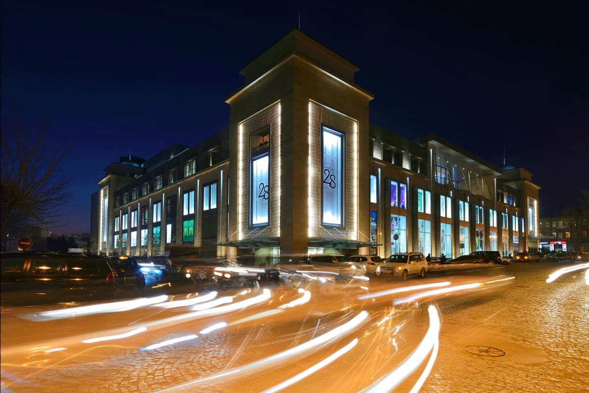 Modern illuminated building with distinctive tower and number 28 at night, with light trails from passing traffic on cobblest
