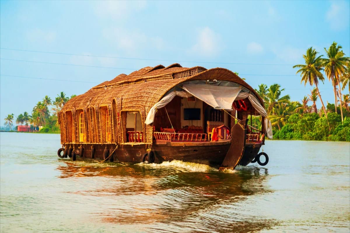 Traditional wooden houseboat with thatched roof floating on calm backwater surrounded by palm trees in Kerala, India
