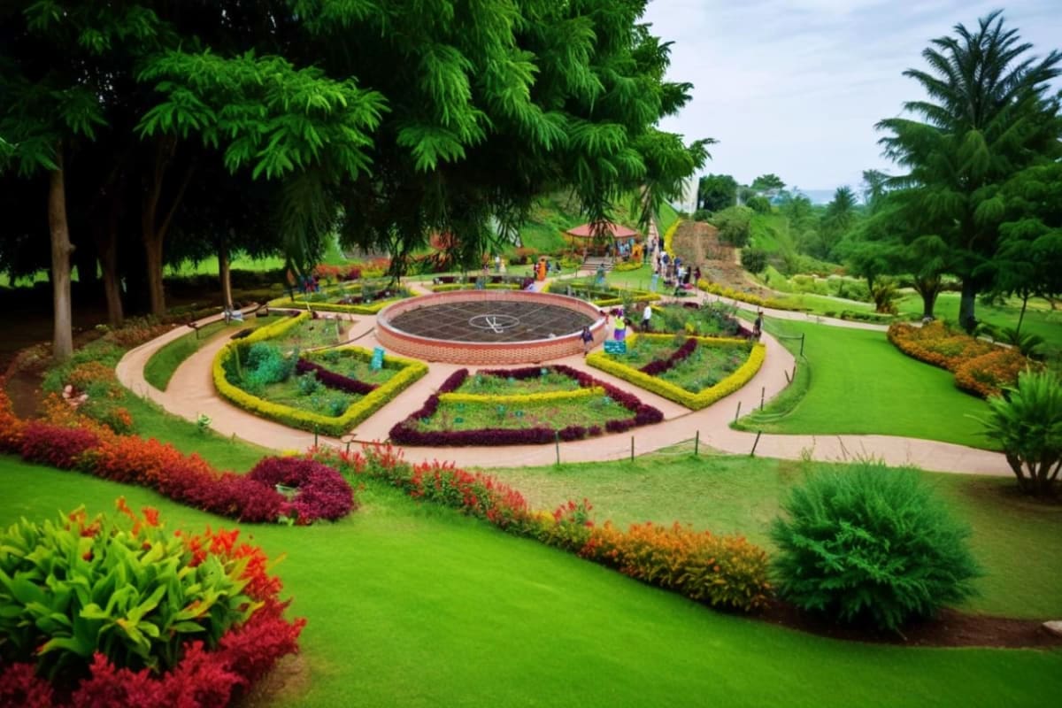 Aerial view of ornamental garden with circular brick sundial feature, colorful flower beds, manicured lawns, and lush green t