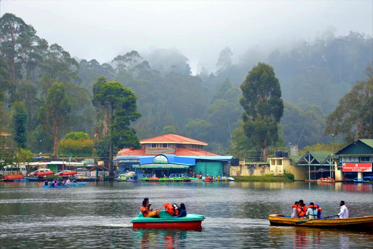 Colorful boats on misty mountain lake with traditional buildings and tall trees in Kodaikanal hill station