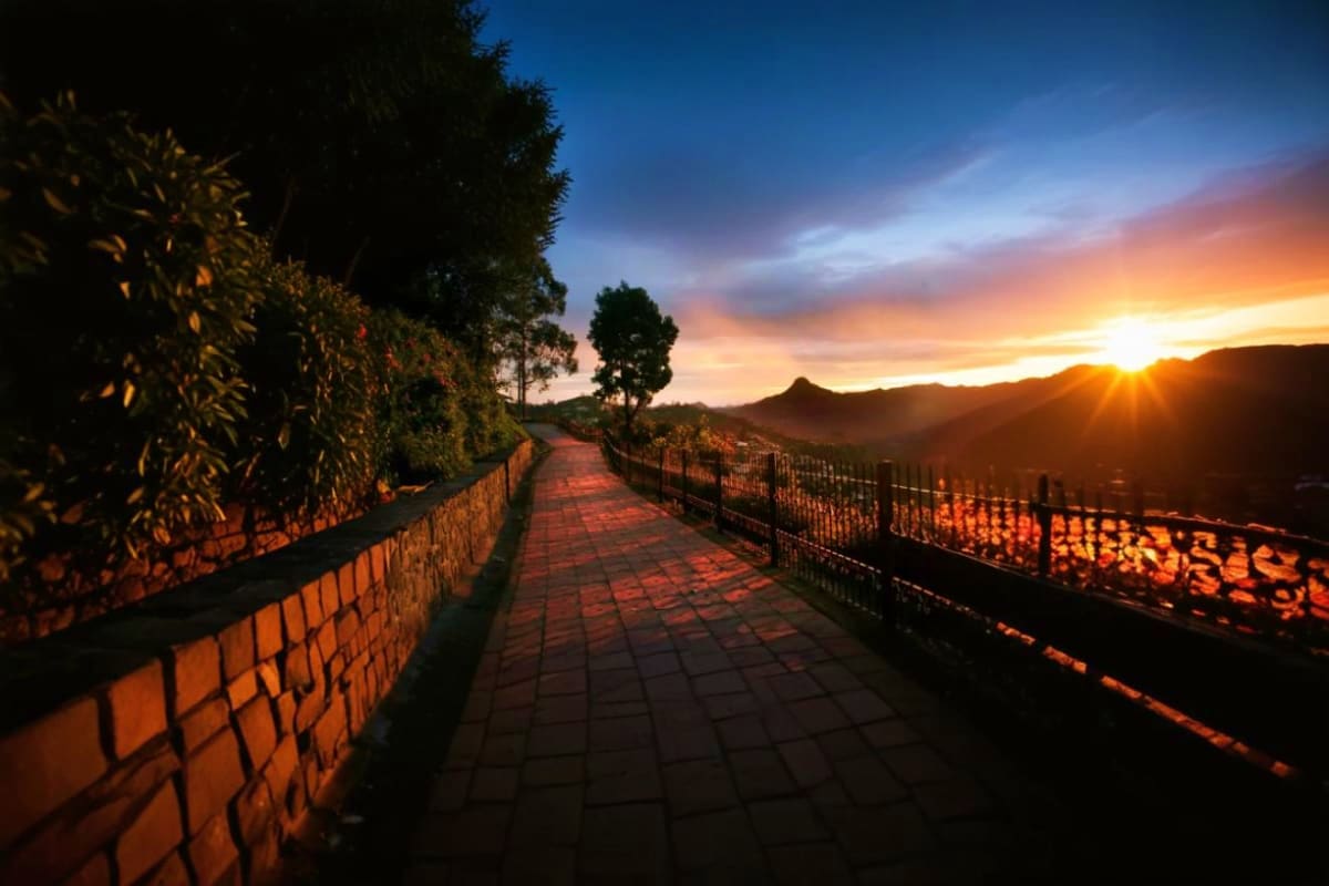 Paved pathway at sunset with stone walls, metal railings, and mountains in the distance during golden hour in Kodaikanal