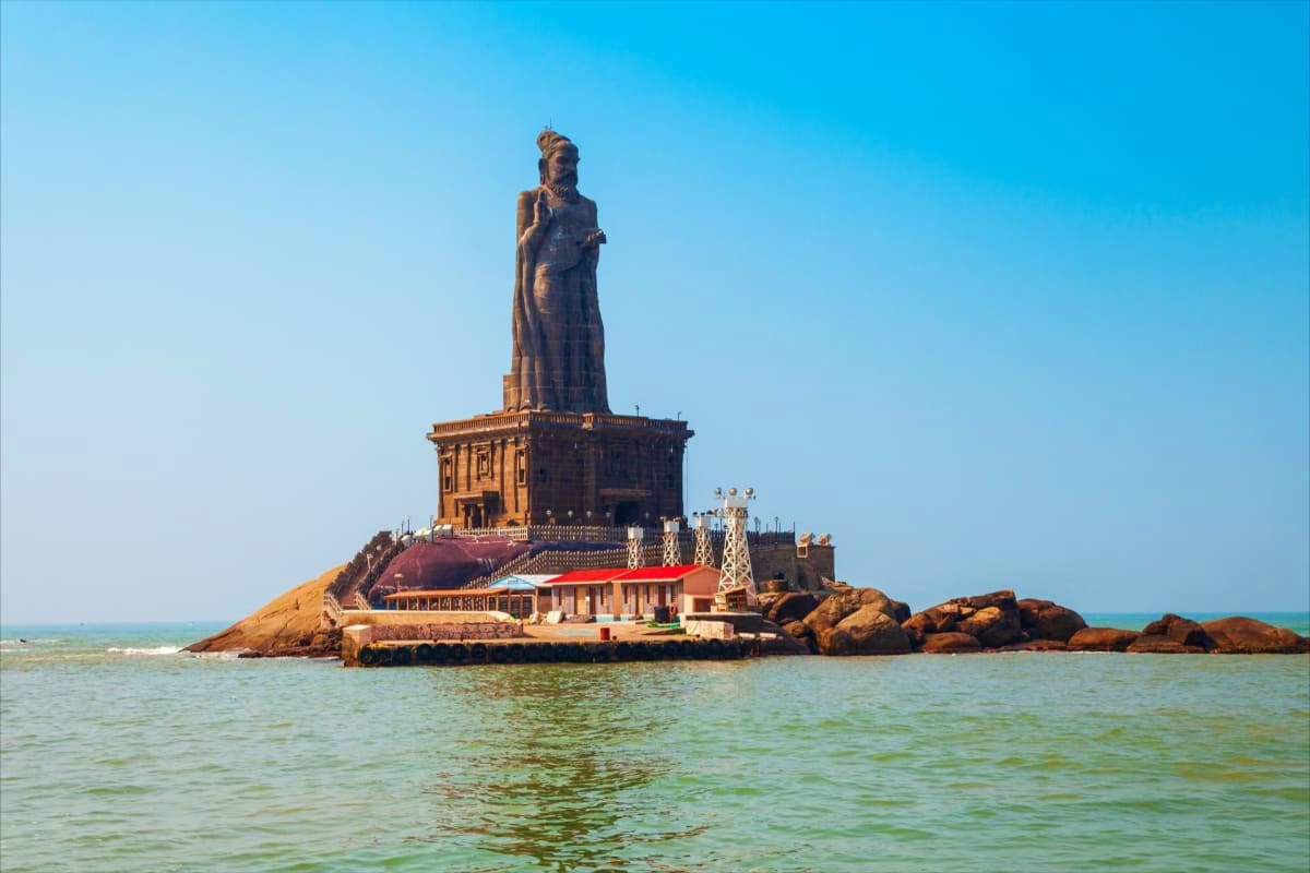 Thiruvalluvar Statue at Kanyakumari with temple base and rocky outcrop surrounded by ocean waters under clear blue sky