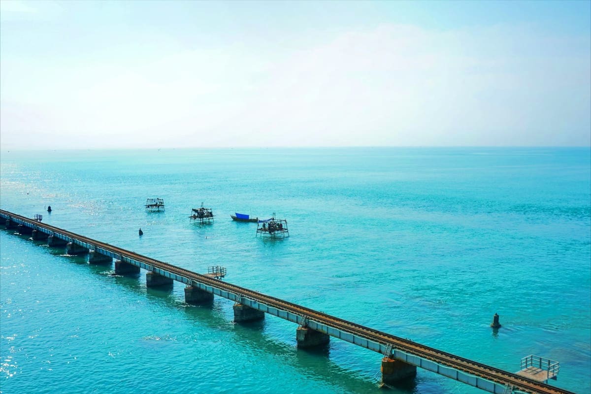 Aerial view of a long pier extending into turquoise ocean water with fishing boats anchored nearby, Rameswaram coastal landsc