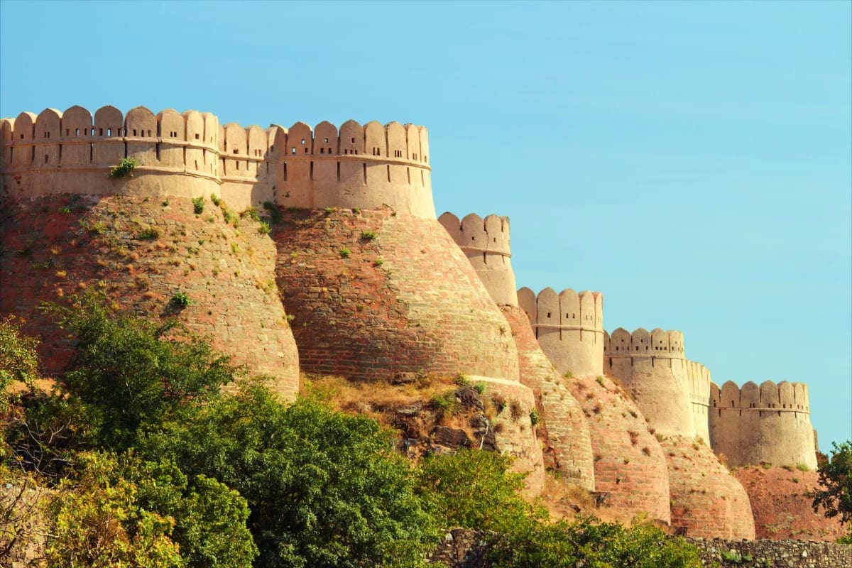 Historic sandstone fort with crenellated walls perched on red rocky hillside against clear blue sky