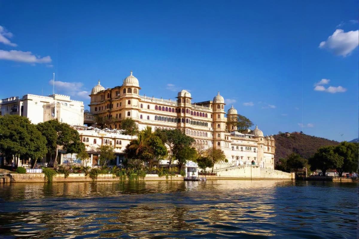 City Palace in Udaipur viewed from Lake Pichola, historic palace with golden domes and cream-colored architecture reflected i