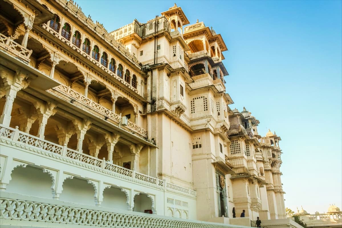 Ornate cream and golden sandstone palace with multiple tiered towers, arched columns, and intricate carved details against cl