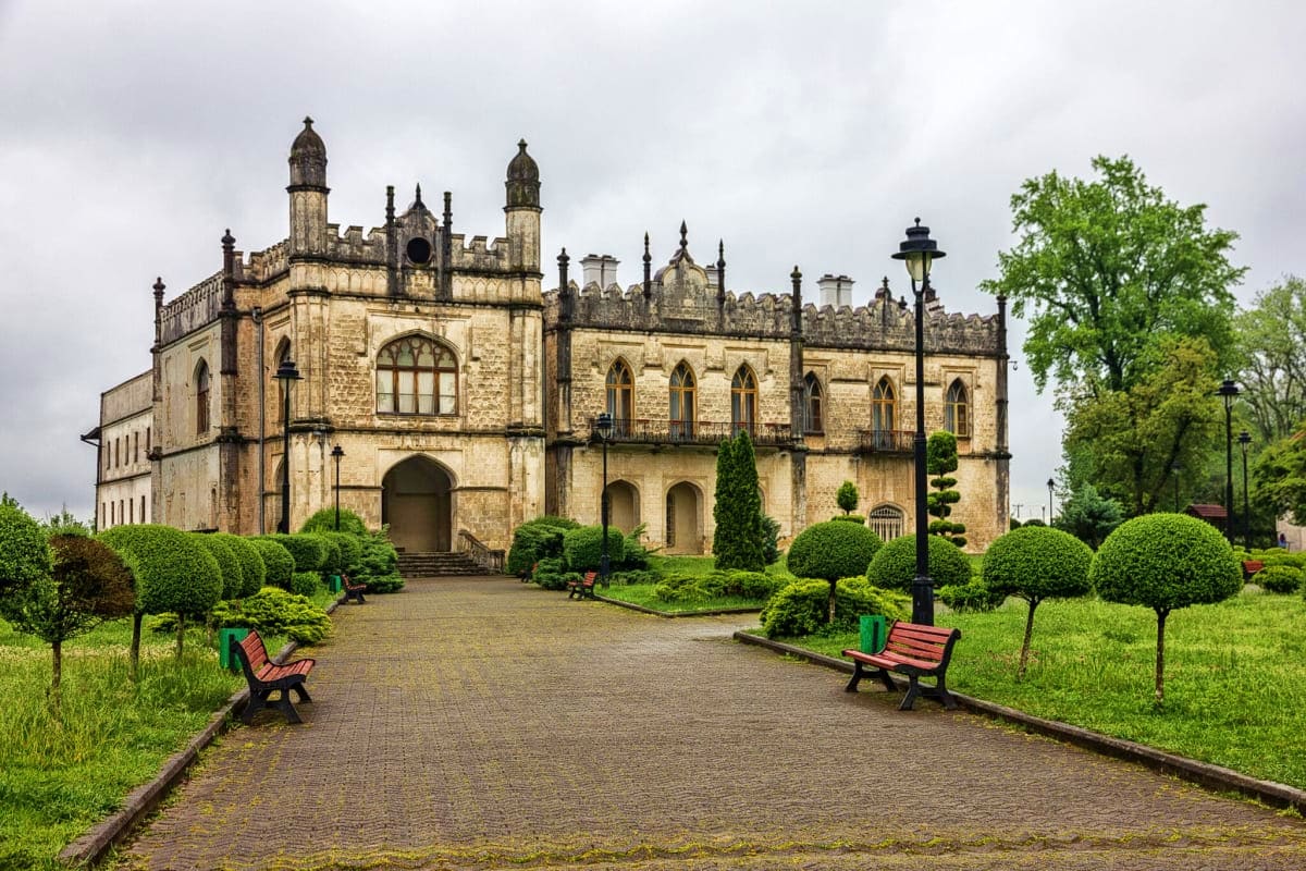 Historic stone castle with Gothic architecture surrounded by manicured gardens and walking paths in Georgia