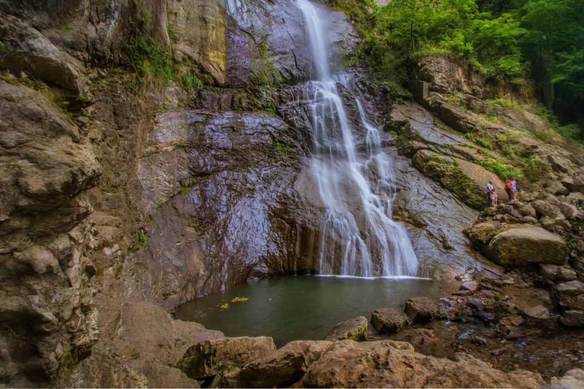 Cascading waterfall flowing into a rocky pool surrounded by moss-covered cliffs and lush green forest in Georgia