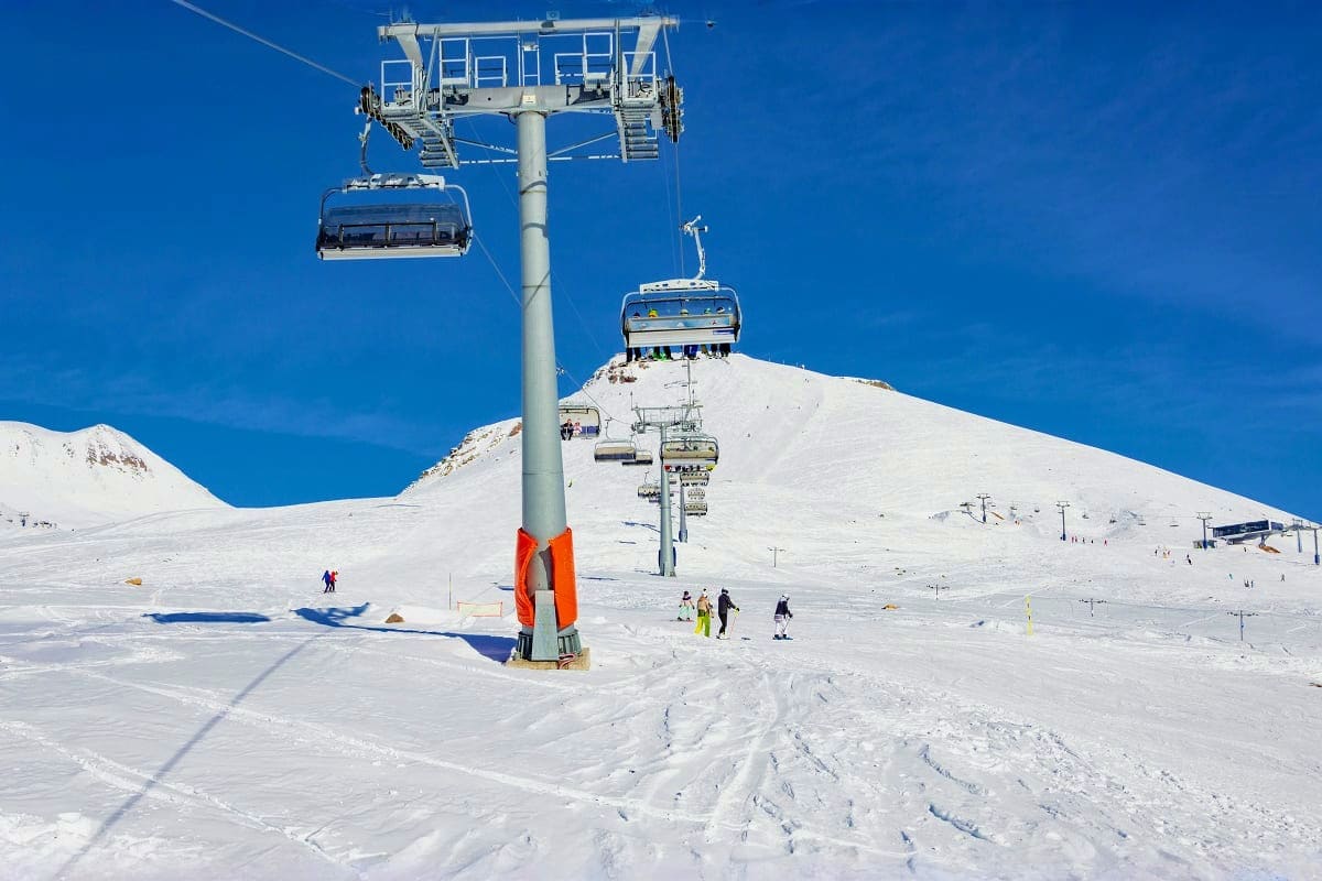 Ski lifts operating on snow-covered mountain slopes with skiers and snowboarders on the white terrain under clear blue sky
