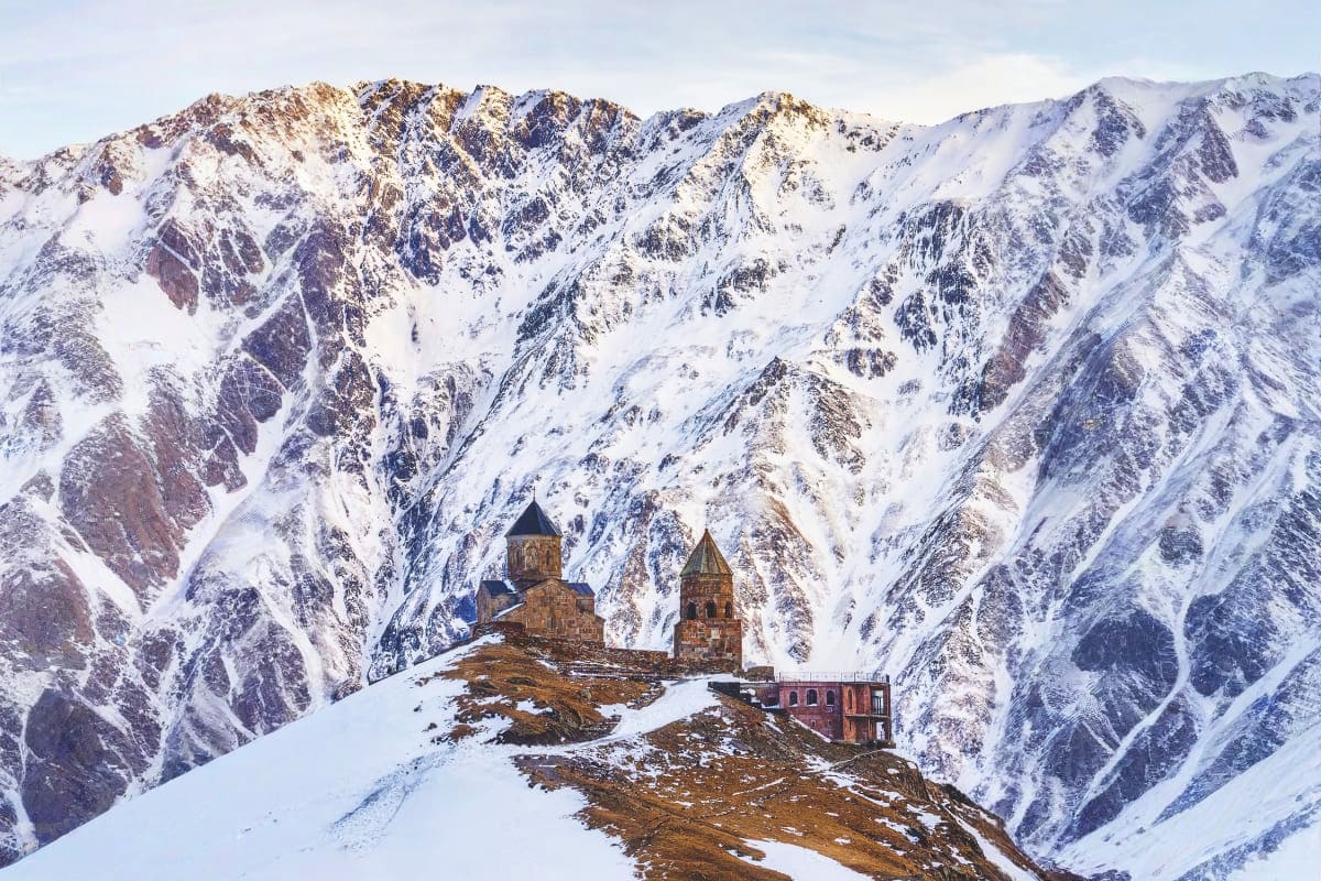 Snow-covered mountains surrounding ancient stone churches with golden domes perched on a rocky ridge in winter in Georgia