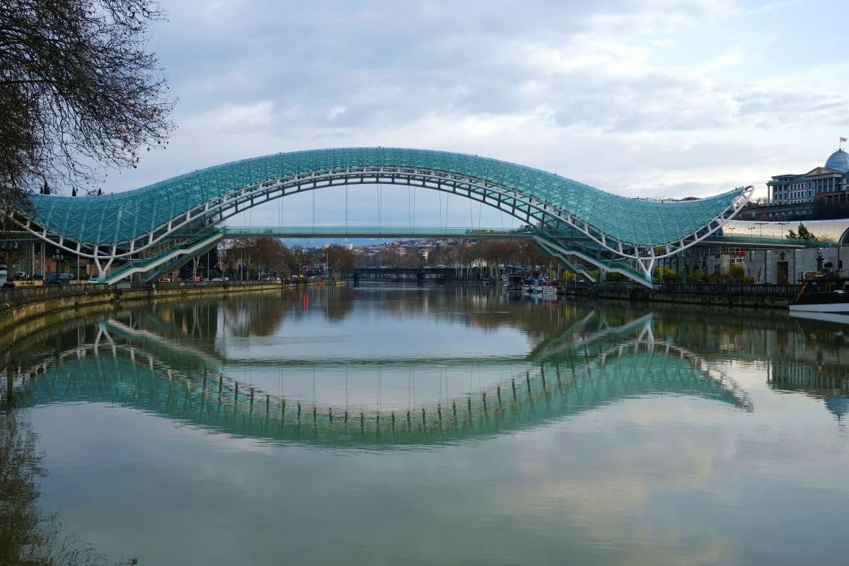 Ailwai Bridge reflected in calm water with turquoise arch design spanning across river in Tbilisi, Georgia