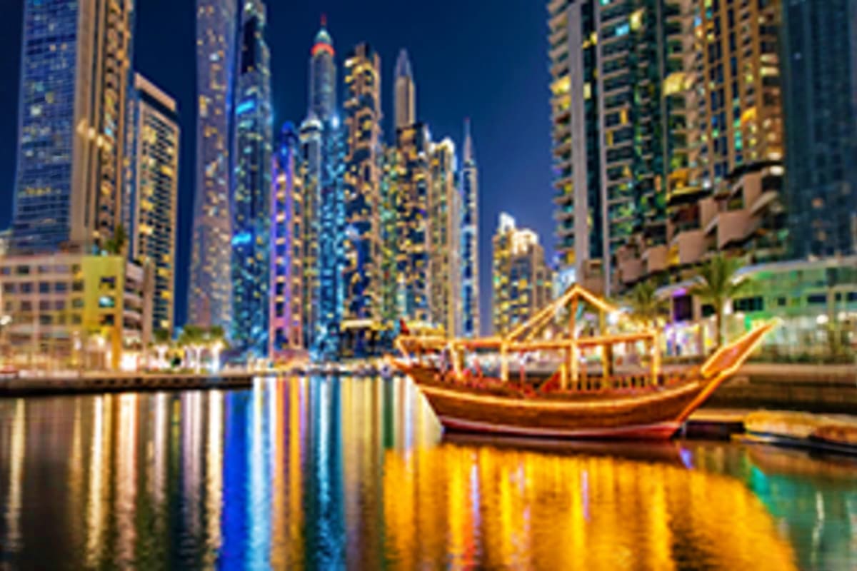 Traditional gold dhow boat moored in Dubai Marina with illuminated skyscrapers reflected in calm water at dusk