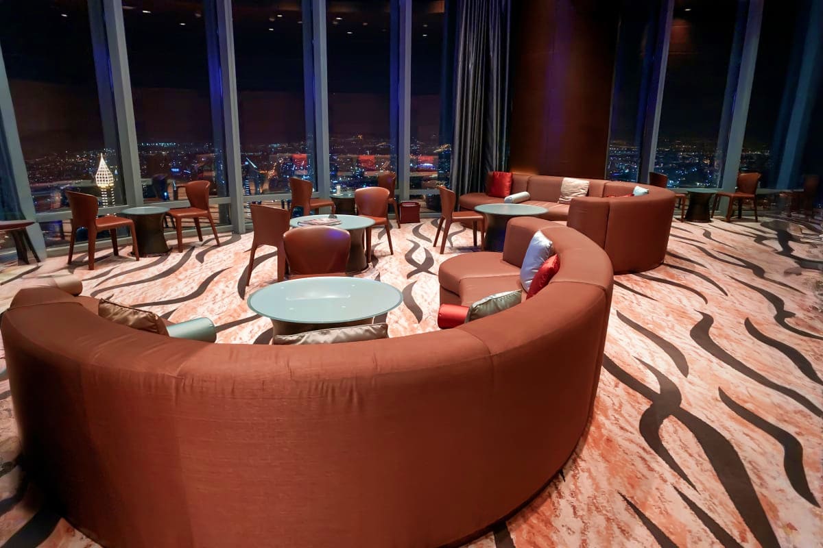 Modern luxury lounge with curved terracotta seating, floor-to-ceiling windows overlooking illuminated Dubai cityscape at nigh