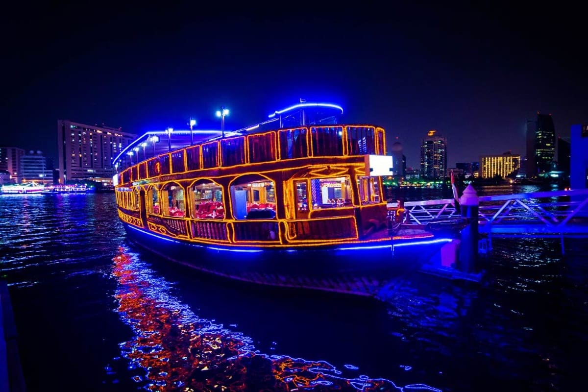 Illuminated traditional abra boat with blue and gold neon lights docked at night on Dubai Creek with city skyline in backgrou