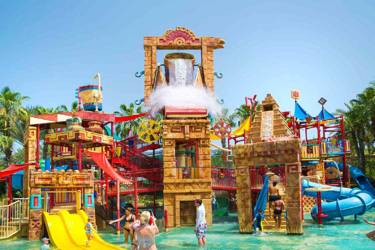 Ancient Egyptian-themed water park attraction with large stone structure, waterfall, colorful slides, and visitors enjoying t