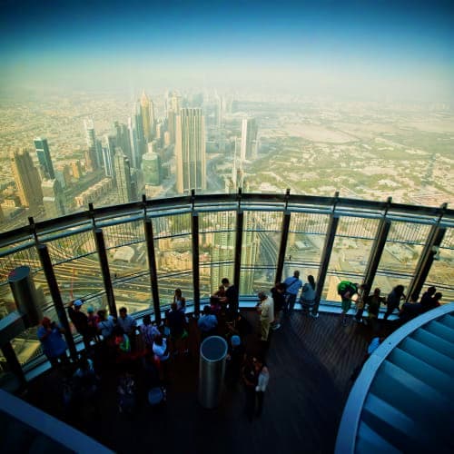 Tourists viewing Dubai skyline from observation deck with downtown buildings and desert landscape visible below