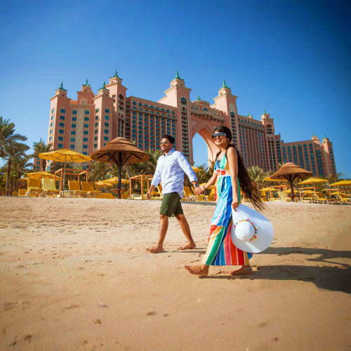 Couple walking on beach with Atlantis The Palm luxury resort hotel in background under clear blue sky