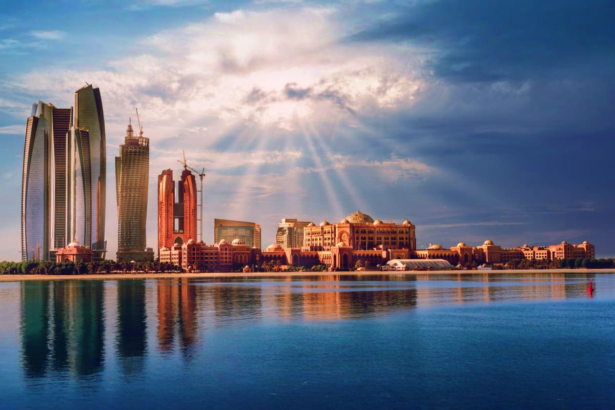 Abu Dhabi waterfront skyline with modern high-rise buildings and traditional architecture reflected in calm blue water at sun